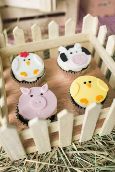 cupcakes with farm animals on them sitting in a wooden box surrounded by straw