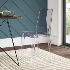 a clear plastic chair sitting on top of a rug next to a table with a vase