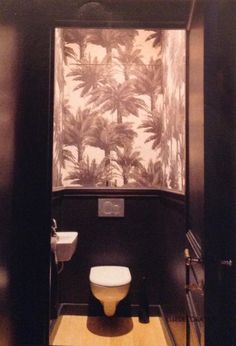 a bathroom with black walls and palm trees on the wall behind the toilet is a shower stall