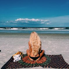 a woman sitting on top of a beach next to the ocean under a blue sky