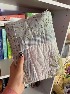 a person holding up a quilted pillow in front of a book shelf filled with books