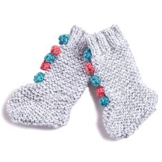 two white knitted mittens with colorful pom - poms on the top