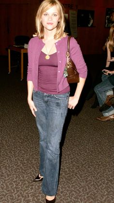 a woman standing in a room with her hand on her hip wearing jeans and a purple cardigan