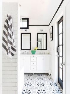 a white bathroom with black and white tile on the floor, two mirrors above the sink