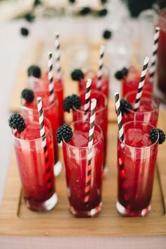 red drinks with blackberries are lined up on a tray and ready to be served