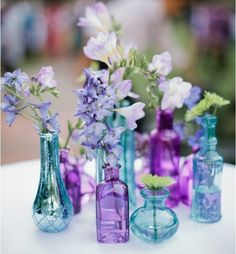 purple and blue vases with flowers in them on a white tableclothed surface