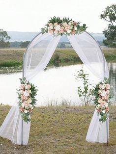 a wedding arch decorated with flowers and greenery by the water in front of a lake