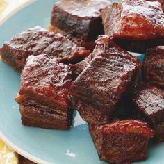 a blue plate topped with cubes of meat on top of a wooden table next to a yellow napkin