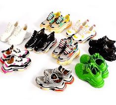 there are many pairs of shoes on the white floor and one is black, yellow, red, green, blue