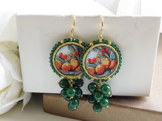 a pair of earrings with green beads on top of a white box next to flowers