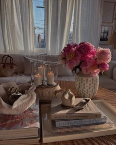 a coffee table topped with books and vases filled with flowers next to a window