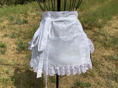 a white lace apron on a mannequin in a field with grass and trees