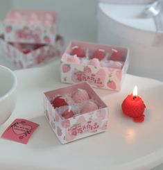 two small boxes filled with candies on top of a white table next to a candle