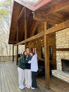 two women hugging each other in front of a log cabin with a fireplace and covered porch