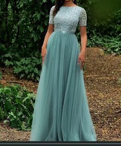 a woman standing in front of some bushes wearing a dress