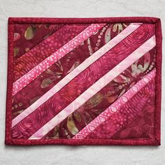 a red and pink quilted placemat on a white surface with stripes in the center