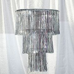 a silver chandelier hanging from a ceiling in front of a white curtain with fringes