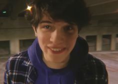 a young man wearing a blue hoodie and looking at the camera with a smile on his face