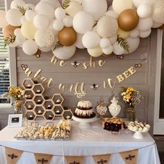 a table topped with lots of desserts next to a wall covered in balloons and honeycombs