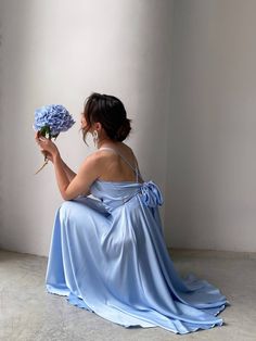 a woman sitting on the floor holding a bouquet of flowers in one hand and wearing a blue dress