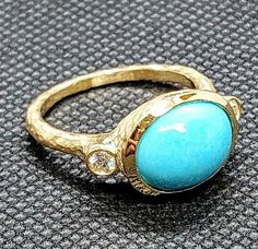 a gold ring with a turquoise stone and diamonds on the bottom, sitting on a gray surface