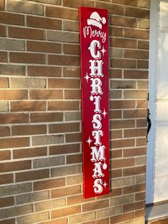 a red sign that says merry christmas hanging from the side of a brick wall next to a white door