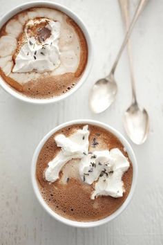 two cups of hot chocolate with whipped cream on top and spoons next to them