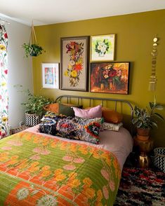 a bed sitting in a bedroom next to two pictures on the wall and plants hanging above it