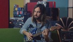 a man with long hair playing an electric guitar in a room full of sound equipment