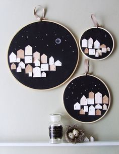 two black and white wall hangings with houses in the night sky on each one