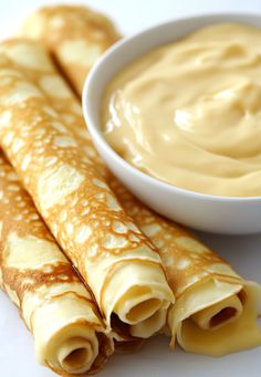 two crepes are next to a bowl of peanut butter on a white surface