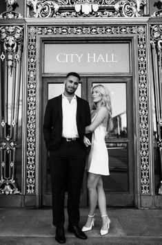 a man and woman standing in front of a city hall entrance with the doors open