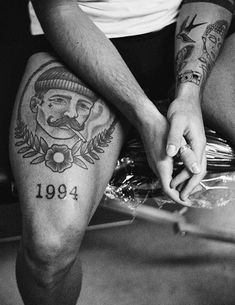 black and white photograph of a man with tattoos on his legs holding the leg of another person