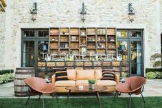 two chairs and a couch in front of a stone building with wine racks on the wall