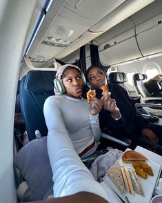 two people sitting in an airplane with food on trays and headphones to their ears