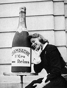 a woman sitting on the ground next to a large bottle of champagne and talking on her cell phone