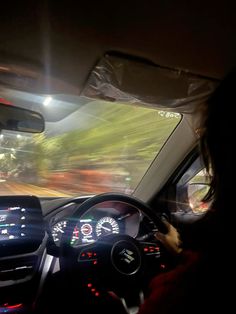 a woman driving a car at night with the lights on and dashboard illuminated by headlights