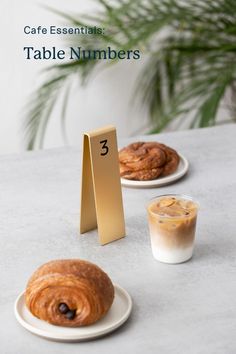 the table numbers are next to two pastries on plates and a cup of coffee