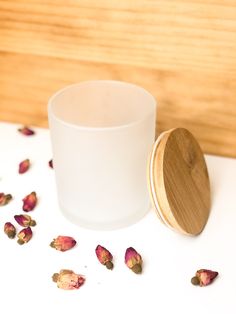 a white cup with rose petals scattered around it and a wooden lid on the table