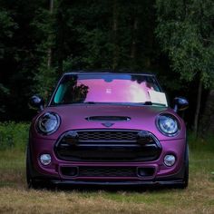 the front end of a purple mini cooper parked in a grassy area next to trees