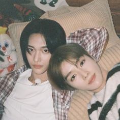 two young men laying on top of a bed next to each other with stuffed animals behind them