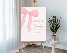 a welcome sign with a pink bow on it next to a potted plant and easel