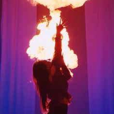 a woman standing in front of a fireball with her hands up to the sky