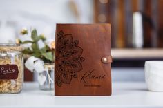 a personalized leather journal sitting on top of a table next to jars and flowers