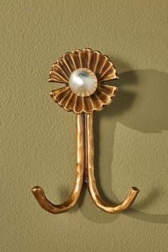 a gold coat hook with a pearl in the center on a green wall behind it