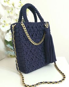 a crocheted bag with a tasseled handle and gold chain hanging from it