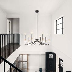 a black and white living room with chandelier in the center, stairs leading up to the second floor