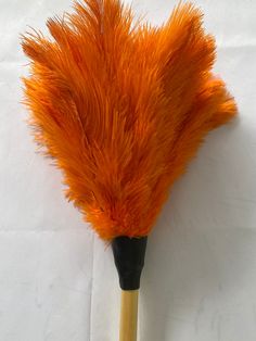 an orange feather duster sitting on top of a white table next to a wooden stick