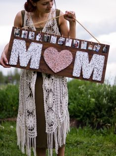 a woman holding a sign with the word mom written on it and pictures hanging from it