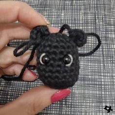 a hand holding a small black crocheted animal with eyes on it's head